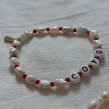 Load image into Gallery viewer, A handmade beaded bracelet featuring irregular white keshi pearls and small red beads, with white letter beads spelling 'COYG' on a textured off-white fabric background.