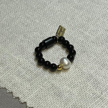 Load image into Gallery viewer, Overhead shot black onyx stretch ring with freshwater pearl, 24k gold vermeil bead and signature Fangirl Unauthorised tag