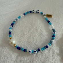 Load image into Gallery viewer, Beaded bracelet with blue, white, and gold beads on a light fabric background
