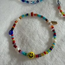 Load image into Gallery viewer, Colorful beaded bracelet with a smiley face charm on a white fabric background
