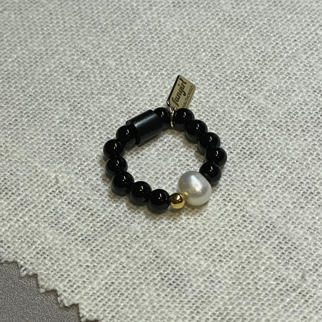 Overhead shot black onyx stretch ring with freshwater pearl, 24k gold vermeil bead and signature Fangirl Unauthorised tag